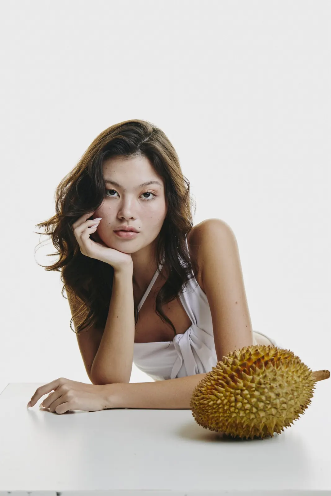 นางแบบนั่งเท้าคางบนโต๊ะขาว มีลูกทุเรียนจริงวางอยู่ข้างหน้า