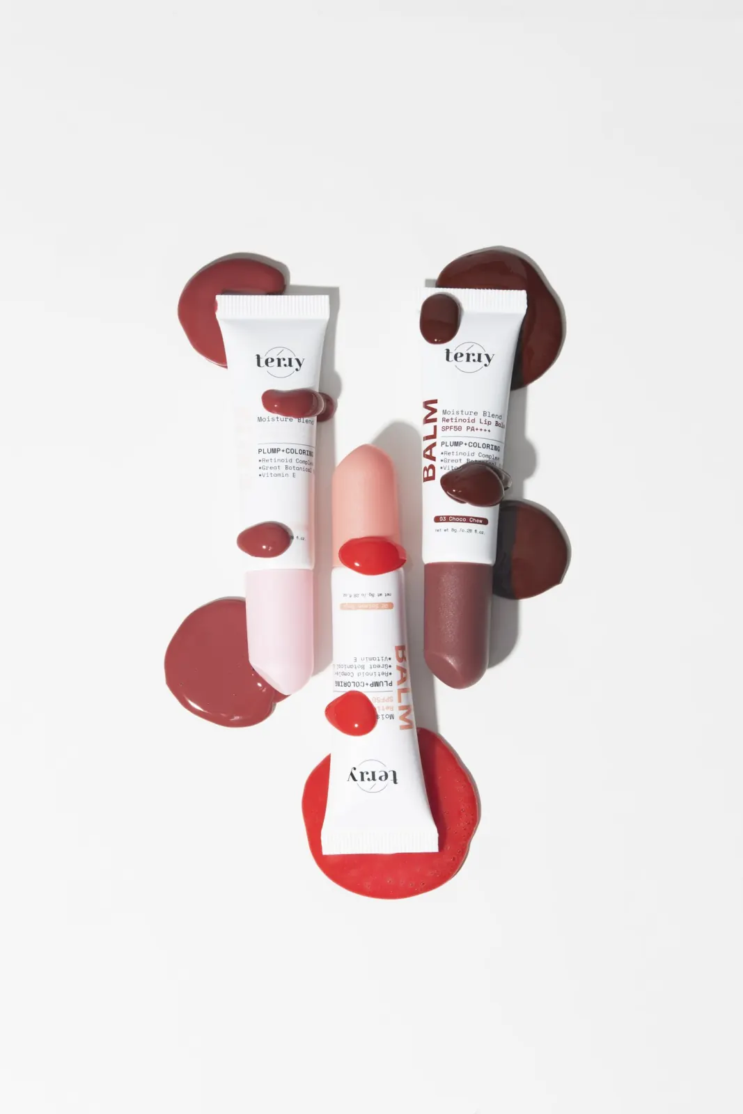 หลอดลิปบาล์มสามหลอดวางกระจายบนพื้นขาว ล้อมด้วยหยดสีลิปสามเฉด